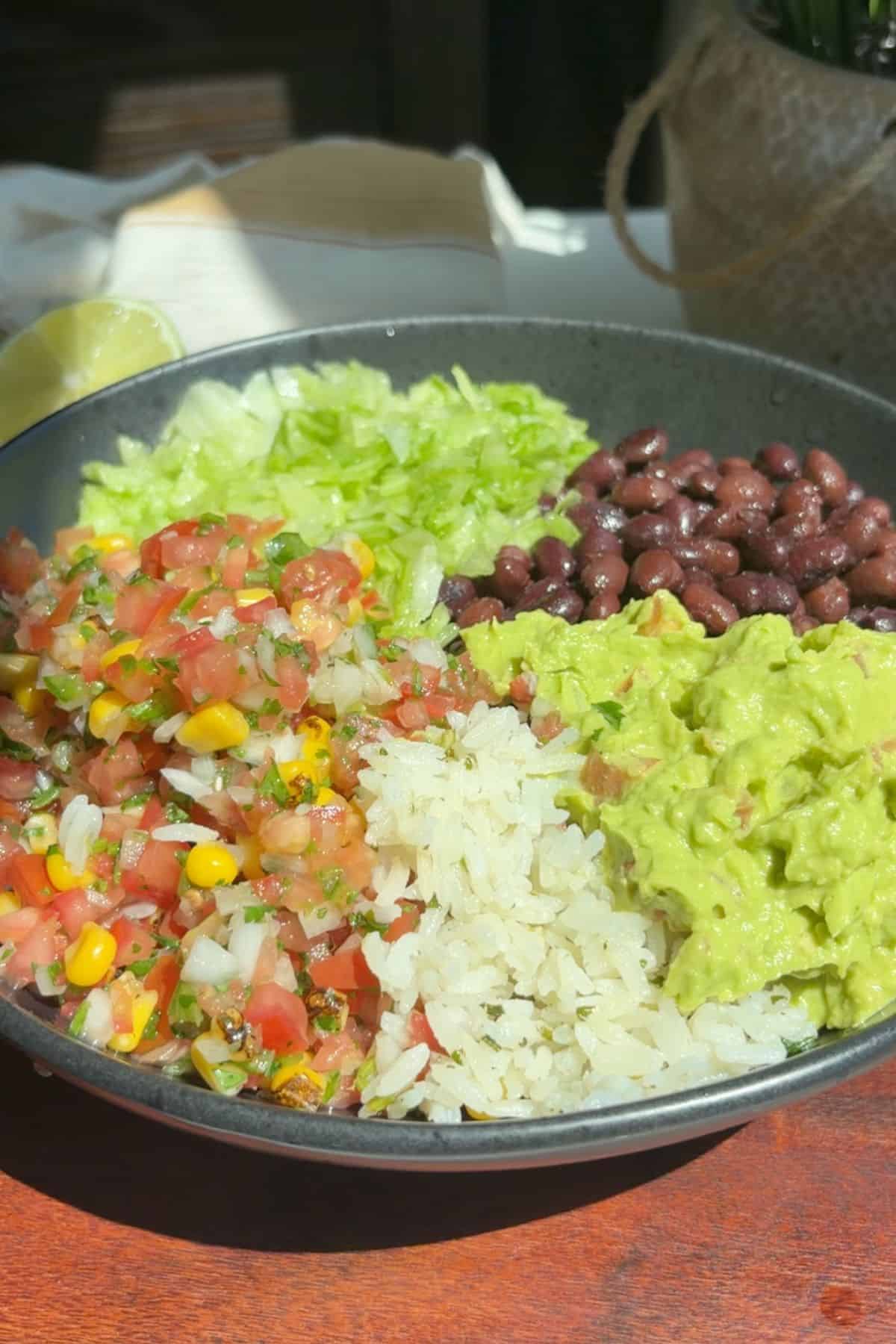 Rice, beans, lettuce, guacamole, and pico de gallo in a bowl.