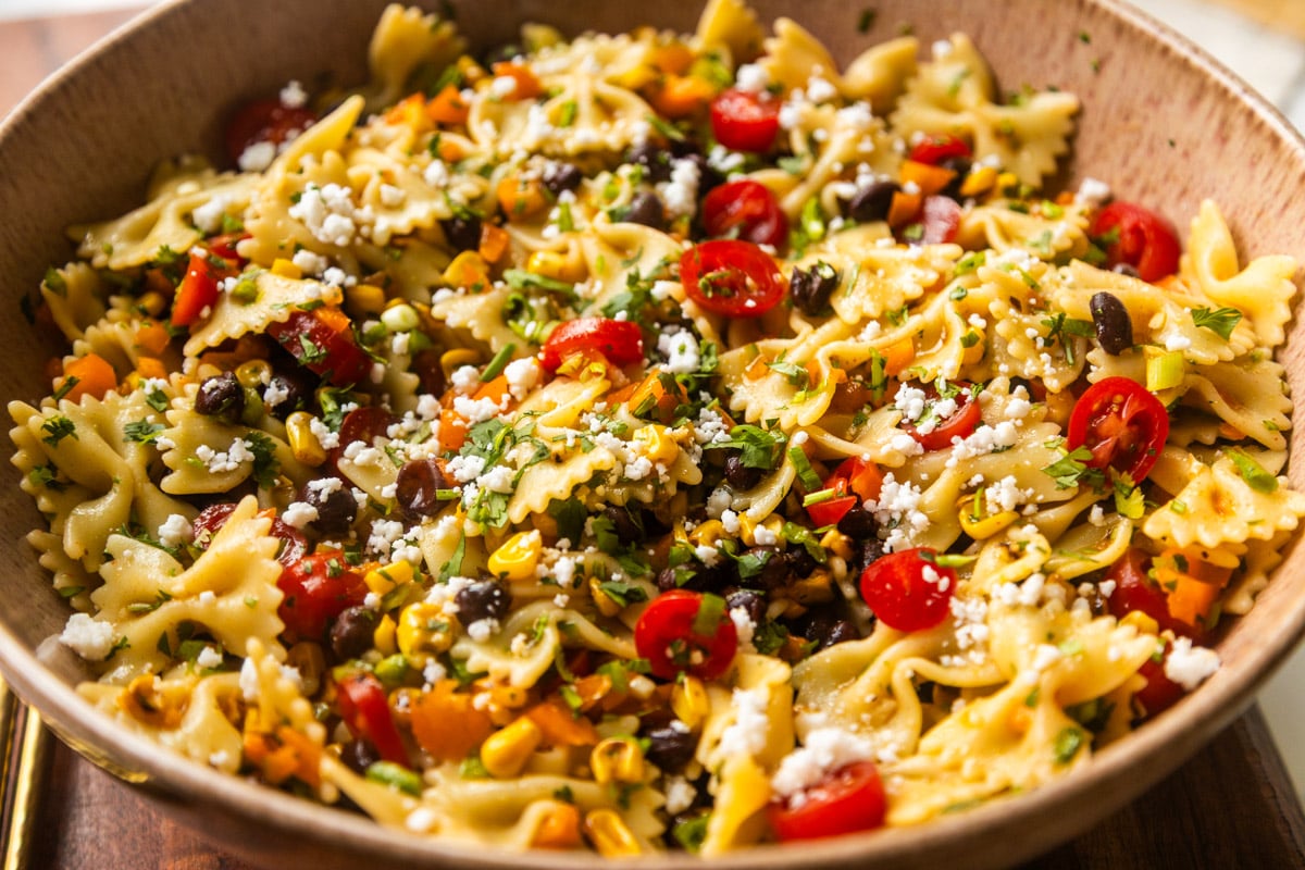 Southwest pasta salad in a bowl on a wooden counter with salad spoons on the side.