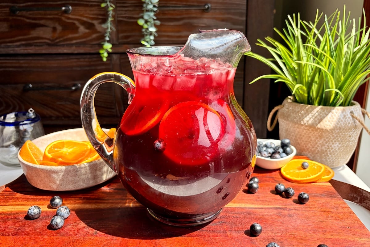 Pineapple hibiscus sun tea in a pitcher topped with sliced oranges.