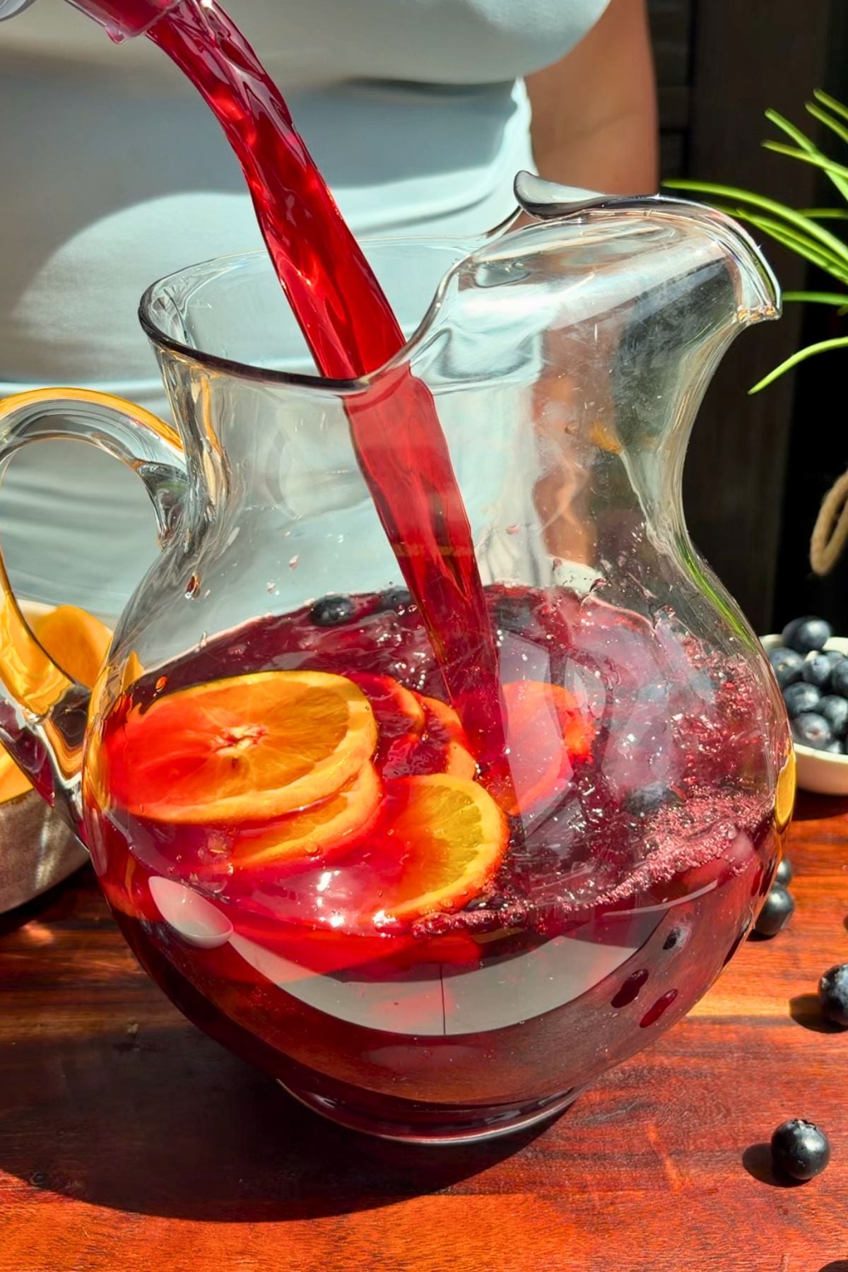 Pineapple hibiscus sun tea pouring into a large glass pitcher with ice.