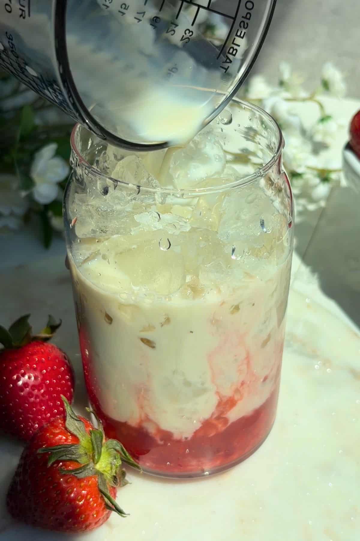 Plant-based milk pouring into a glass with strawberry puree and ice.