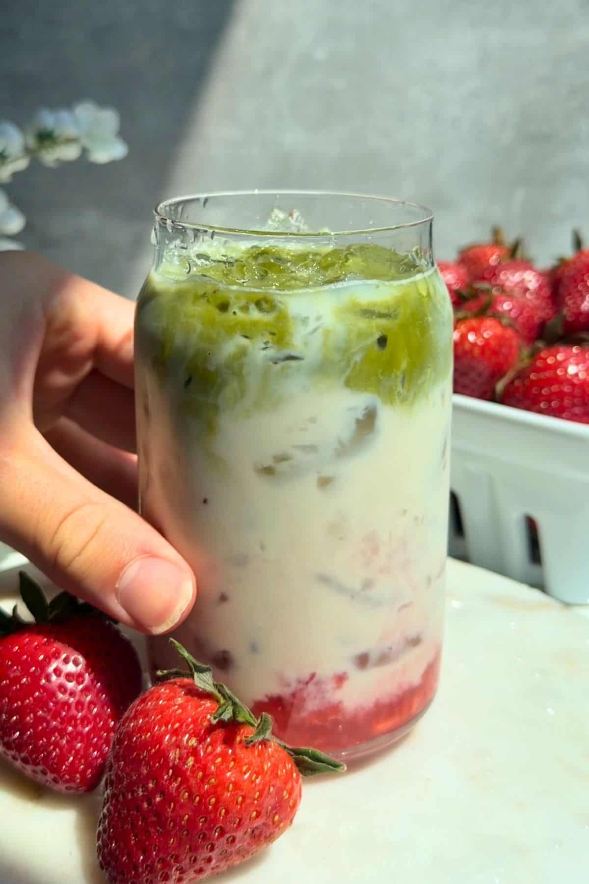 Hand holding up a glass of strawberry matcha latte.