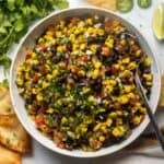 Black bean and corn salsa dip in a white bowl with chips and cilantro on the side.