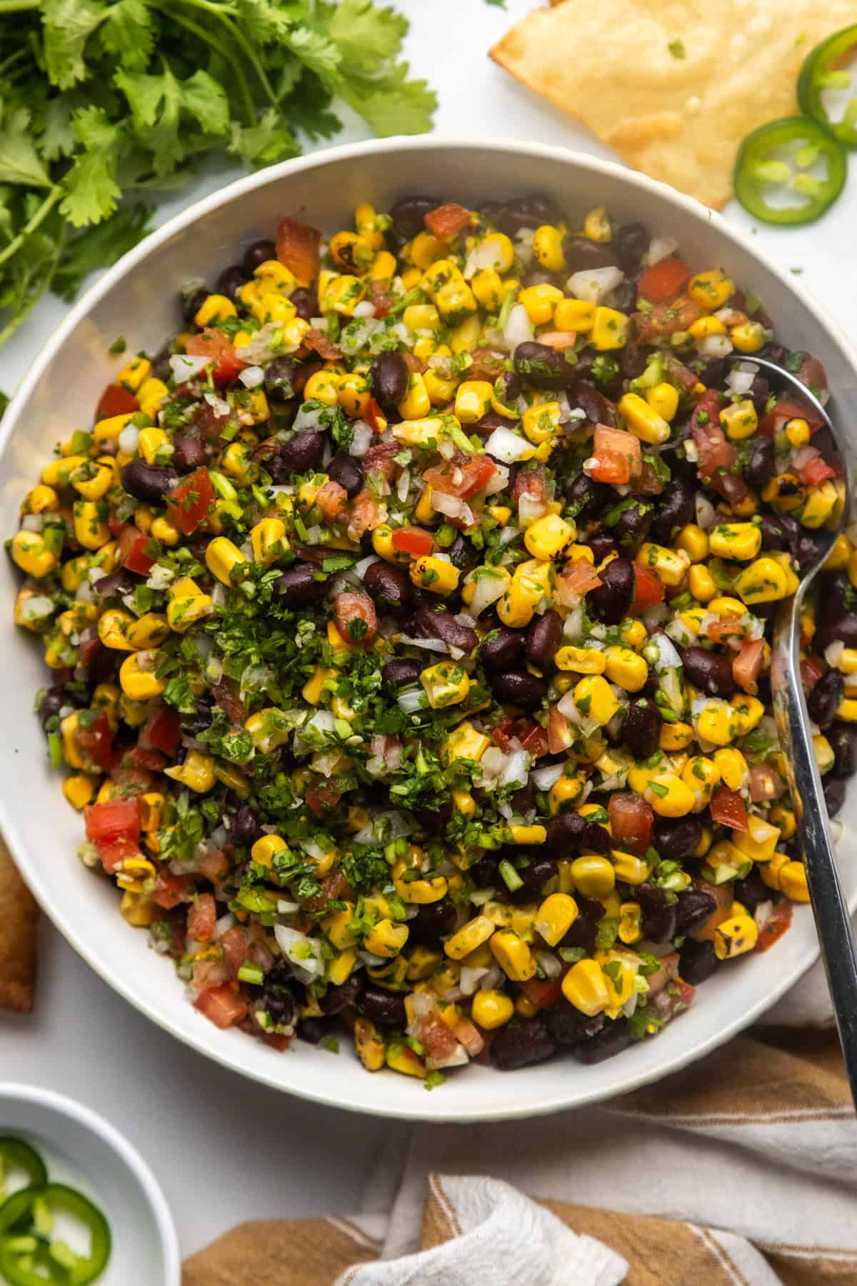 Black bean and corn salsa dip in a bowl with chips and cilantro on the side.