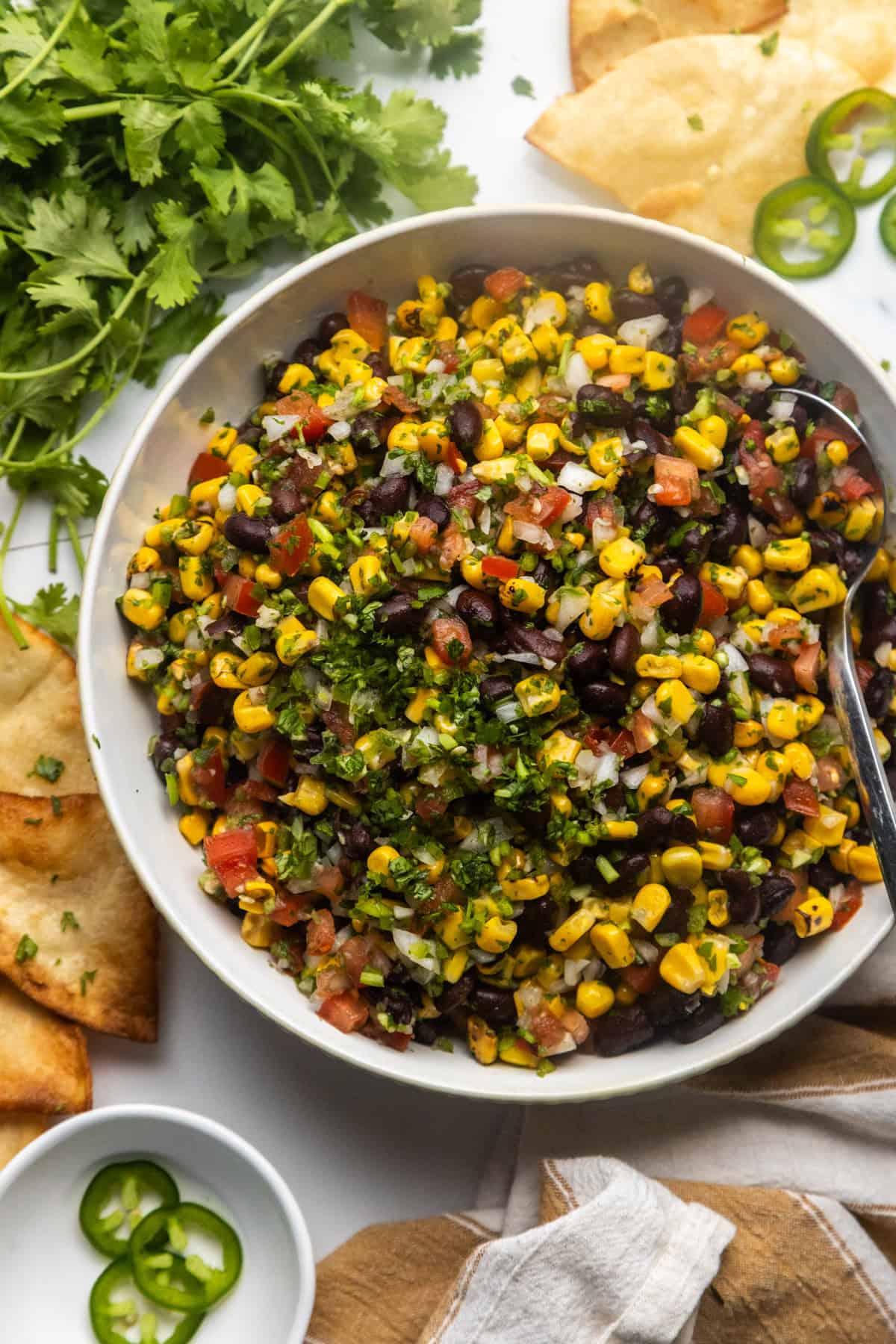 Black bean and corn salsa dip in a serving bowl with chips and cilantro on the side.