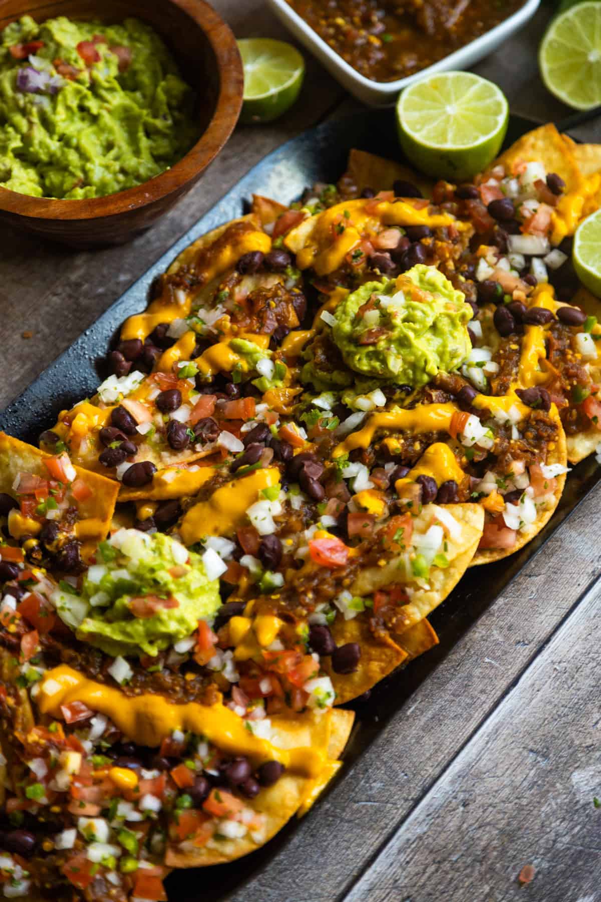 Easy vegan loaded nachos recipe served on a comal with guacamole, salsa, and fresh limes on the side.
