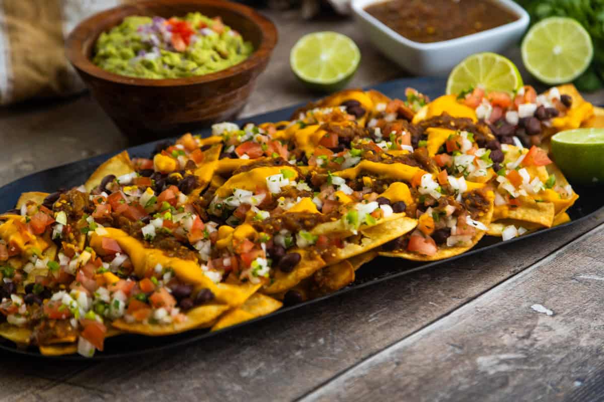 Vegan loaded nachos on a comal with guacamole and salsa on the side.